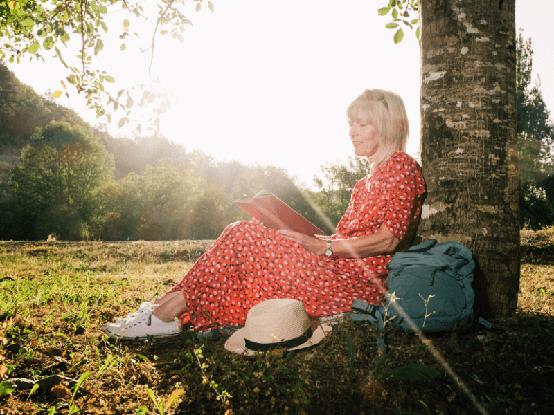 Eine erwachsene Frau sitzt unter einem Baum und liest.